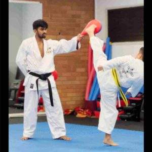 FitDojo Child performing a kick on a high-held kick pad with guidance from their sensei during a karate class.