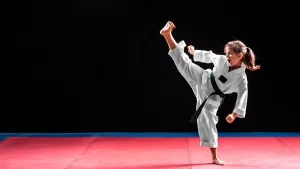 Young girl performing a high karate kick with focus and precision during a taekwondo class.